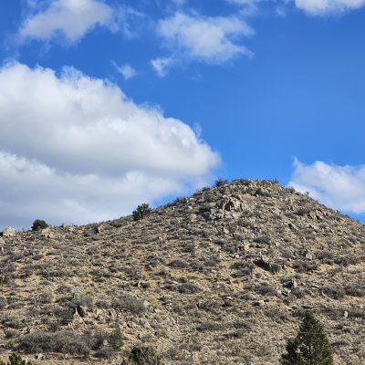 Rocky hill under blue sky with clouds.
