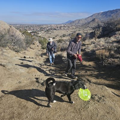 Hiking with dog carrying frisbee in desert landscape.