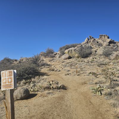 Desert hiking trail sign under clear blue sky.