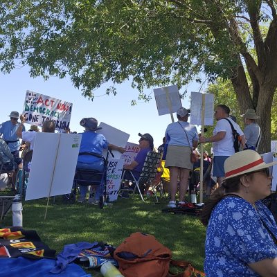 Group of people holding protest signs under a tree.