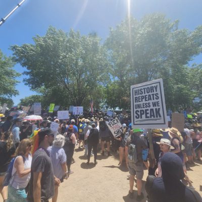Crowd of protesters holding signs in sunny park.