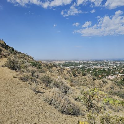Desert trail overlooking a distant cityscape, sunny day.